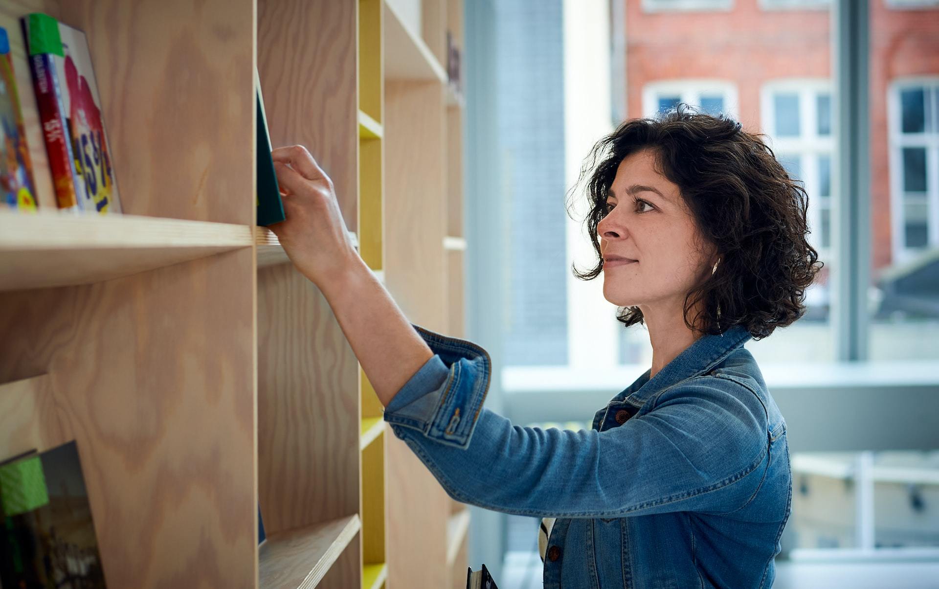 Young woman in blue jacket choosing a book from a bookshelf.