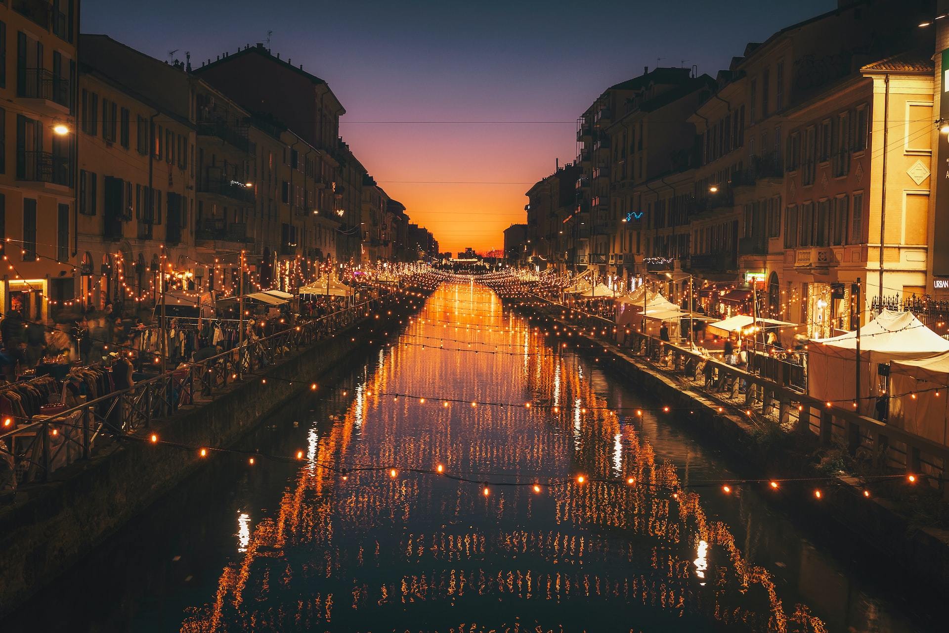 A series of string lights over a canal cast their reflection in the waters below on a bustling night in Milan.