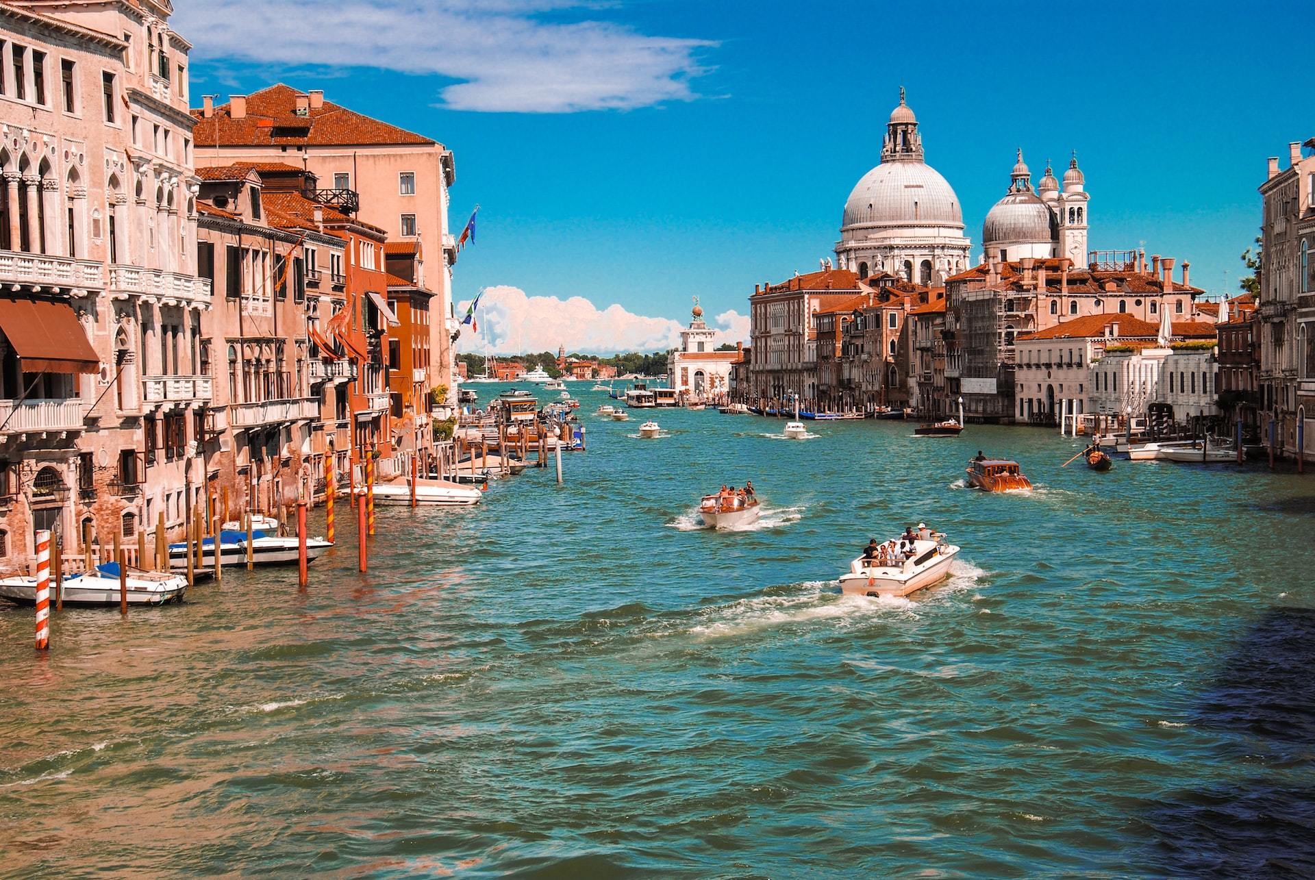 A lineup of boats navigate a canal in Venice during the day.
