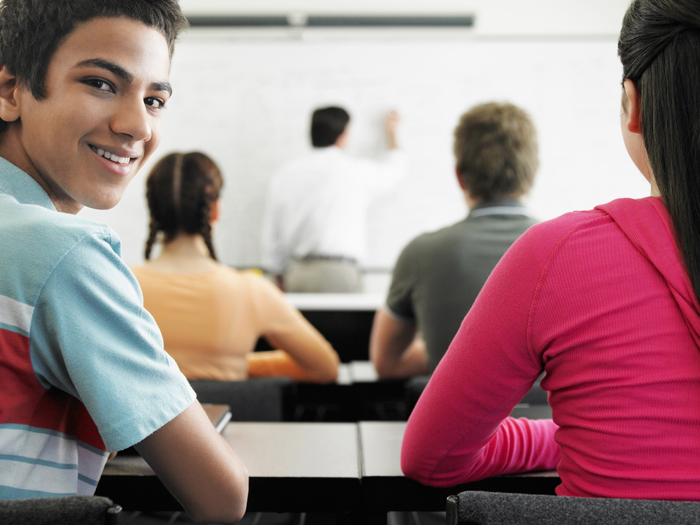 Portrait of happy teenage boy attending lecture in classroom.