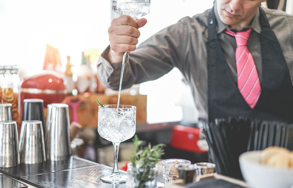 Bartender preparing cocktail with gin, rosemary, and pink pepper inside vintage bar.