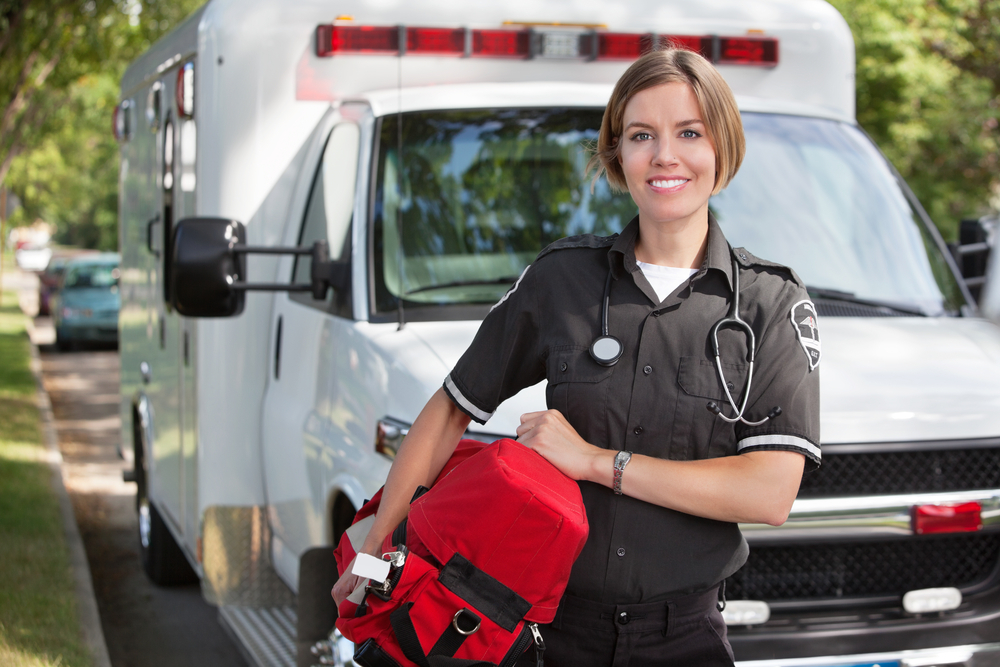 Portrait of a happy paramedic carrying a portable red oxygen unit in front of an ambulance parked on the street.